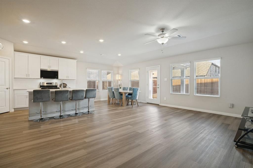 Open-concept interior featuring wood-finish flooring, white shaker-style cabinetry, a central kitchen island, recessed lighting, and a ceiling fan Open-concept interior featuring wood-finish flooring, white shaker-style cabinetry, a central kitchen island, recessed lighting, and a ceiling fan