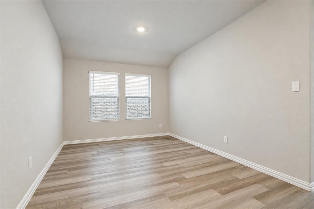 Neutral-toned interior space featuring wood-finish flooring, vaulted ceiling, and dual double-pane windows