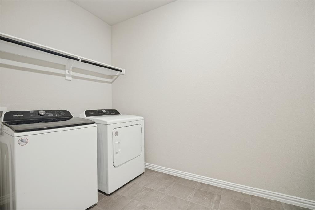 Laundry area featuring tile flooring, neutral wall paint, and an installed overhead storage shelf
