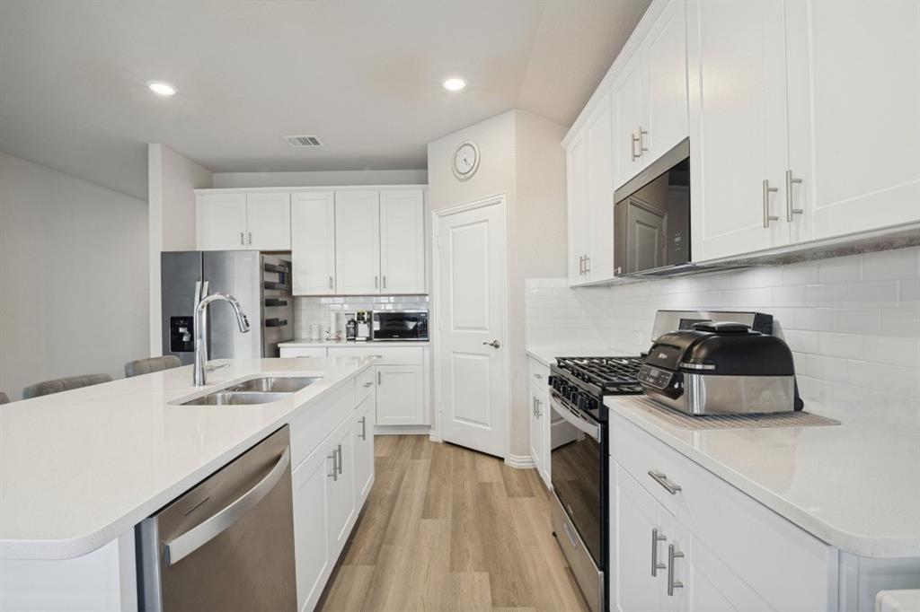 Kitchen featuring white shaker-style cabinetry, solid-surface countertops, subway tile backsplash, stainless steel appliances, and wood-finish flooring