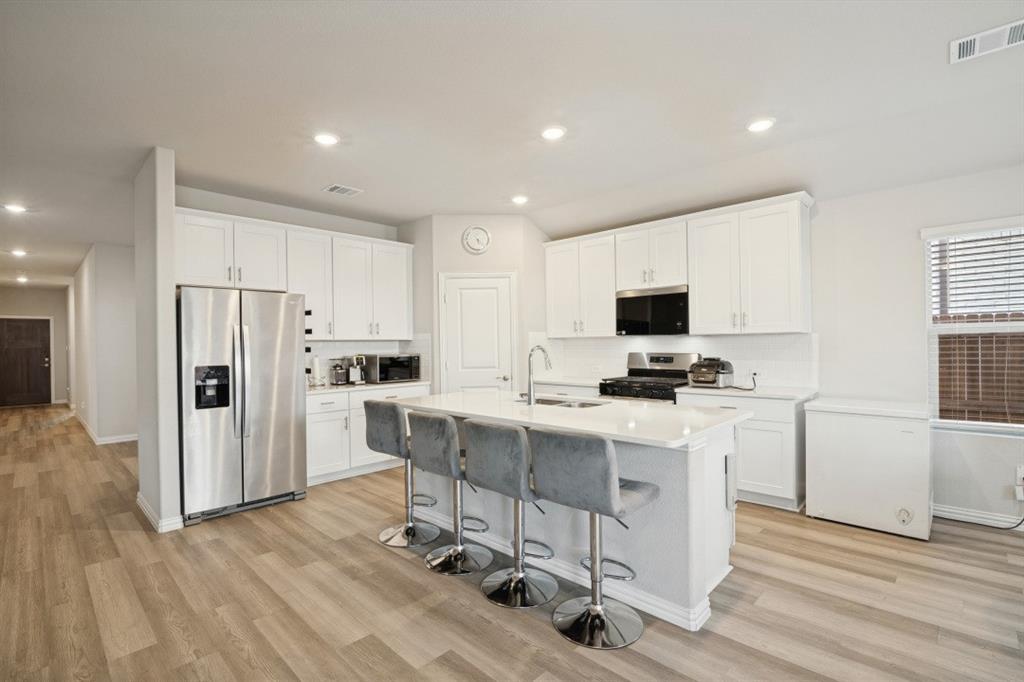 Kitchen featuring white cabinetry, center island with stone-finish countertop and integrated sink, stainless steel refrigerator, and wood-finish flooring Kitchen featuring white cabinetry, center island with stone-finish countertop and integrated sink, stainless steel refrigerator, and wood-finish flooring