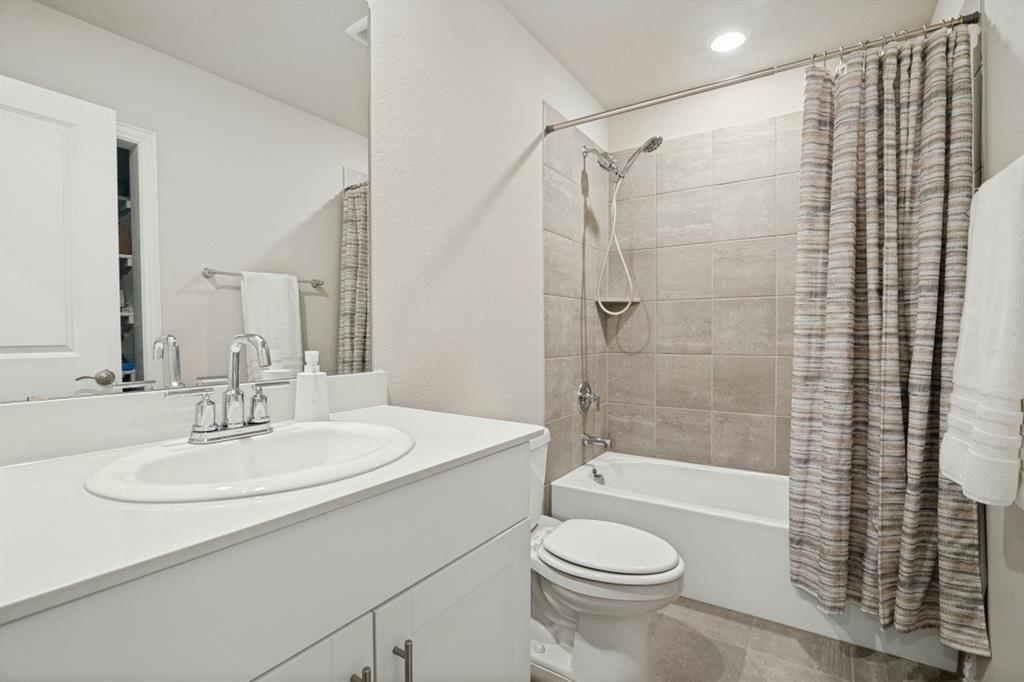 Bathroom featuring a vanity with a solid-surface countertop, an integrated sink, a full-width mirror, a tub-shower combination with tile surround, and a handheld shower fixture