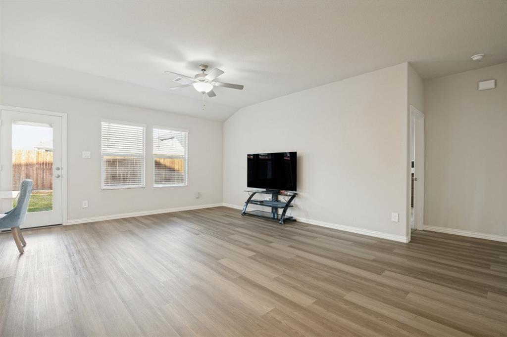 Neutral-toned interior featuring wood-finish flooring, a ceiling fan with integrated lighting, dual windows with blinds, and a glass-paneled exterior door Neutral-toned interior featuring wood-finish flooring, a ceiling fan with integrated lighting, dual windows with blinds, and a glass-paneled exterior door