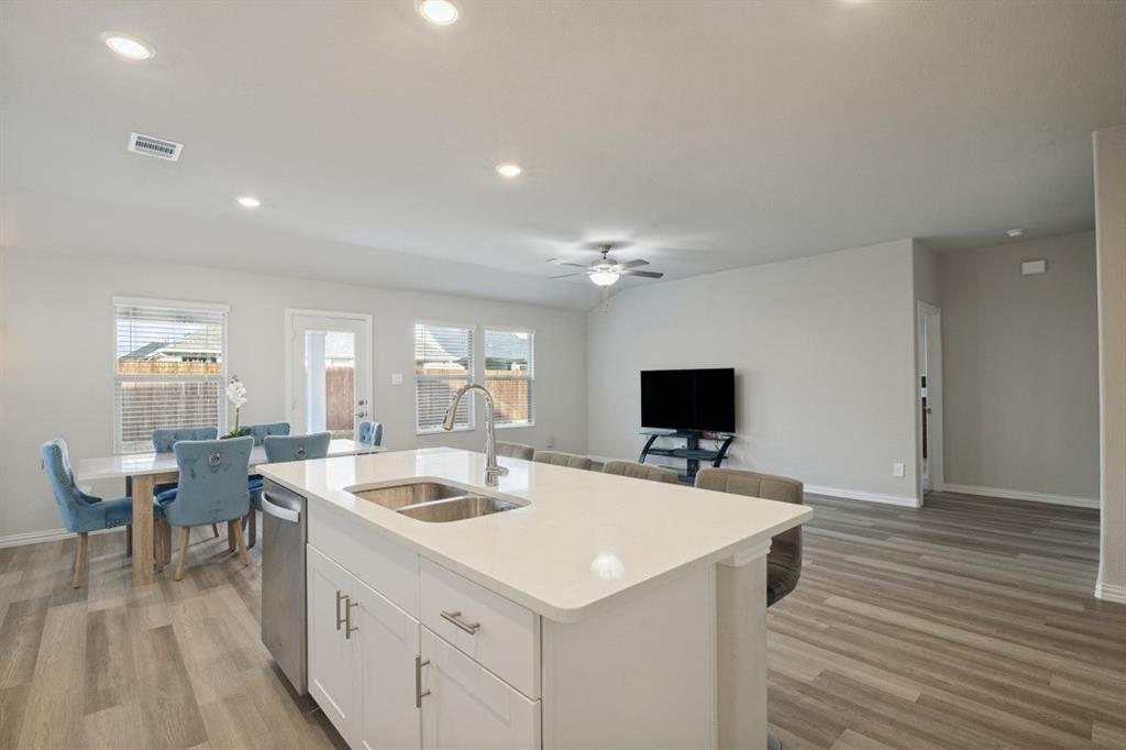Kitchen island with stone countertop, stainless steel dual-basin undermount sink, white shaker-style cabinetry, recessed lighting, and wood-finish flooring
