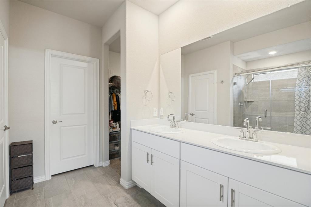 Dual vanity with white cabinetry, rectangular solid-surface countertop, integrated sinks, full-width mirror, and tiled shower surround with glass enclosure
