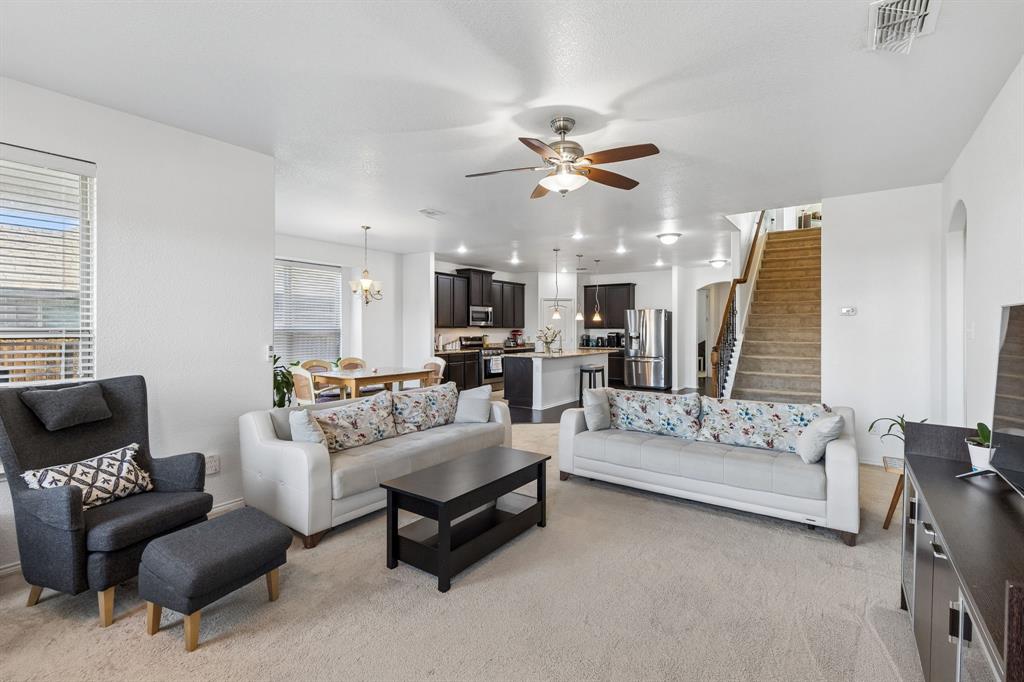 Open-concept living area with carpet flooring and a ceiling fan, featuring a dining area with a chandelier, and a kitchen with dark cabinetry, stainless steel appliances, and a central island with pendant lighting