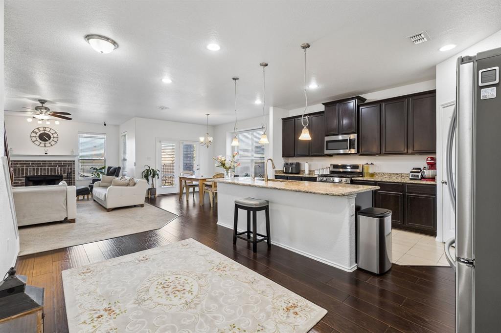 Open-concept design featuring wood-finish flooring, a kitchen island with seating, dark wood cabinetry, and stainless steel appliances