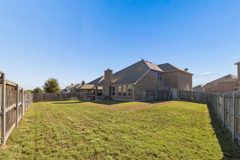 Expansive backyard featuring a manicured lawn, full perimeter fencing, and a brick-clad exterior