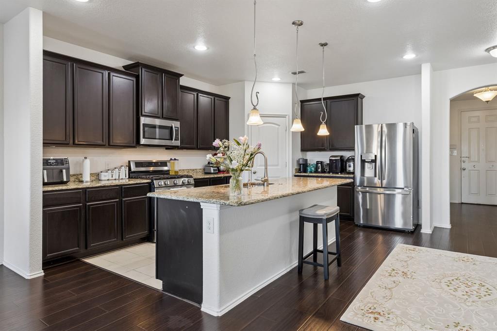 Kitchen featuring dark wood-finish cabinetry, stainless steel appliances, a center island with granite countertop, and wood-finish flooring