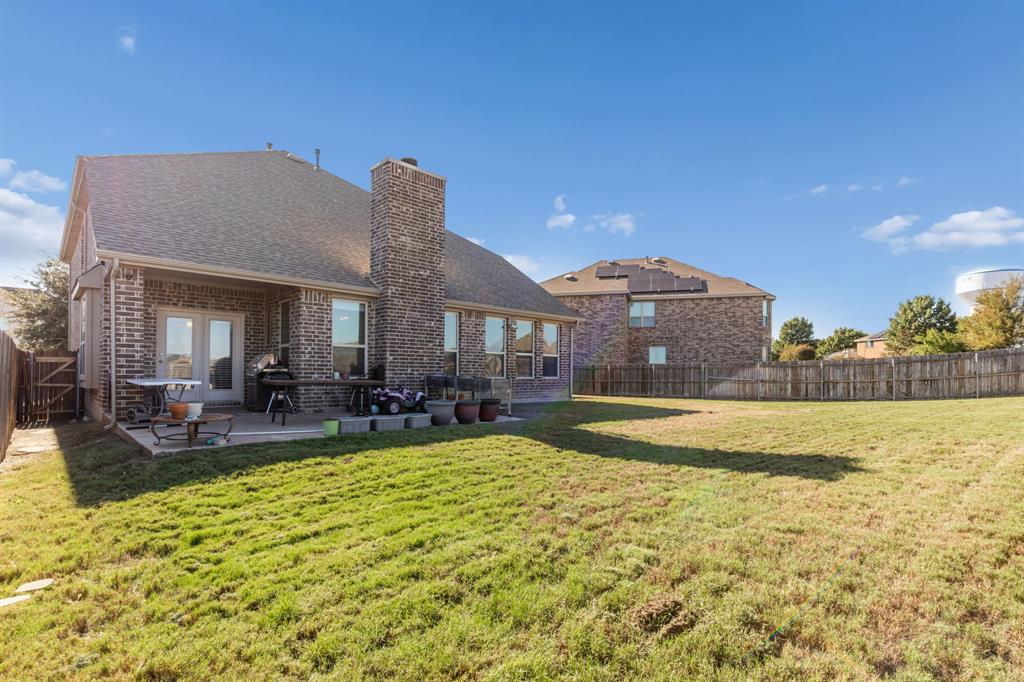 Expansive backyard with a manicured lawn, full brick exterior, covered patio, and dual French doors
