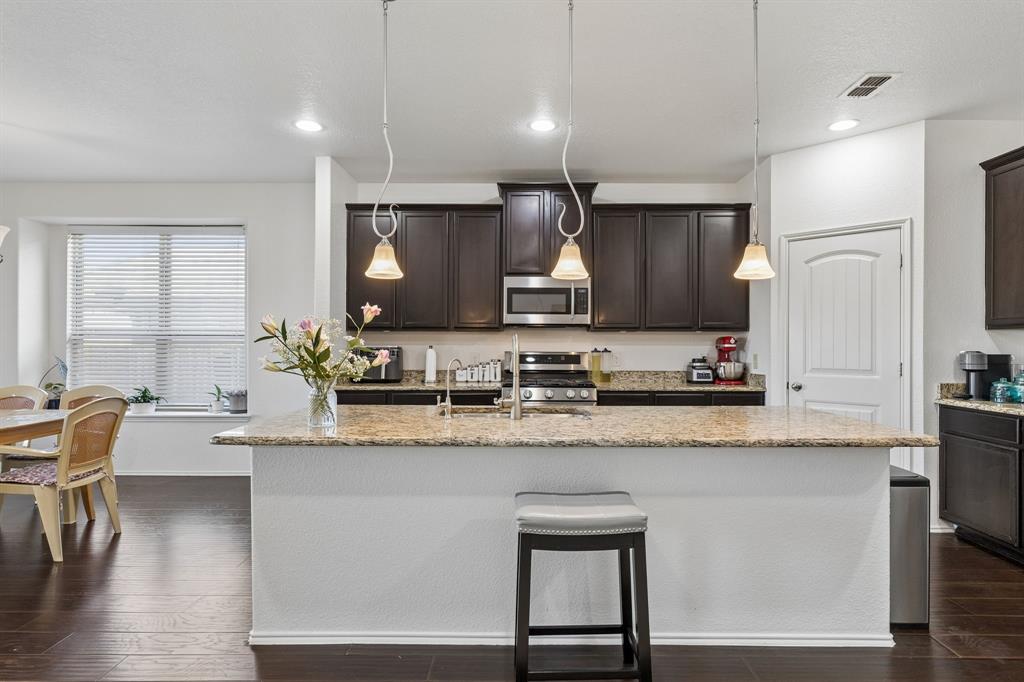Kitchen featuring dark wood-finish cabinetry, stainless steel appliances, granite countertops, and a central island with pendant lighting