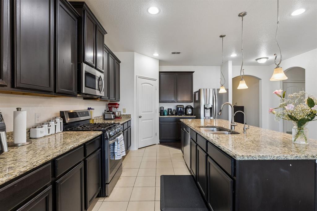 Kitchen featuring dark wood cabinetry, granite countertops, stainless steel appliances, tile flooring, and pendant lighting