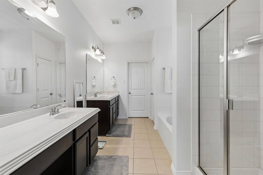 Dual vanities with white countertops, tiled flooring, a glass-enclosed shower, and a built-in bathtub