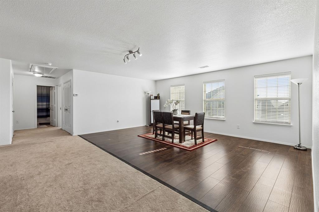 Spacious open-concept room featuring wood-finish flooring, multiple windows with blinds, track lighting, and neutral wall paint