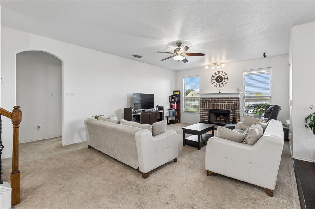 Spacious living area featuring a brick fireplace, ceiling fan, and arched doorway