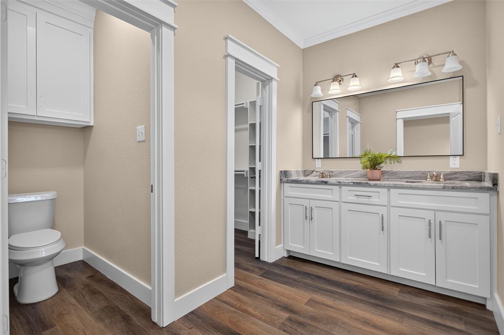Main Bathroom featuring a white double-sink vanity with stone countertop, large rectangular mirror, multi-bulb wall lighting, and wood-finish flooring