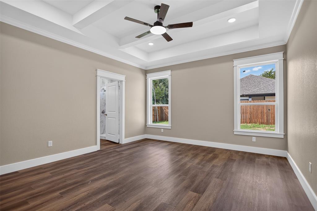 Tray ceiling featuring white crown molding and integrated recessed lighting, wood-finish flooring, two large windows with wide casing, and a dark-finish ceiling fan with integrated lighting