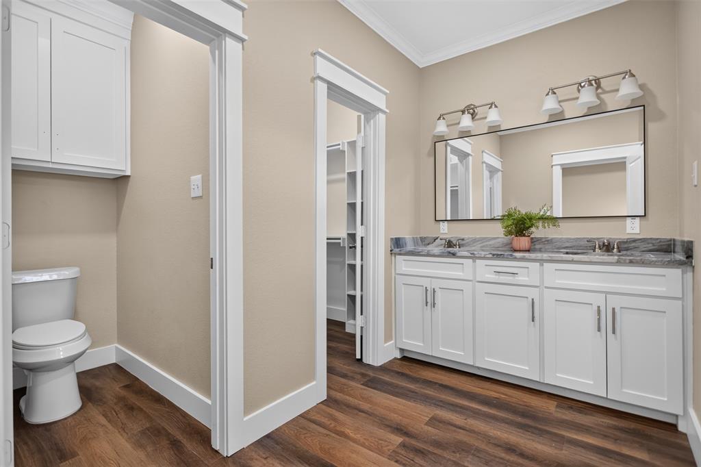 Double vanity with integrated sinks, white shaker-style cabinetry, large rectangular vanity mirror, stone-finish countertop, and wood-finish flooring