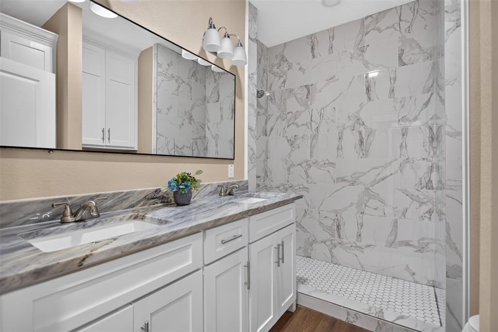 Double vanity with white cabinetry, stone-patterned countertop, under-mount sinks, and a large-format tile walk-in shower with hexagonal floor tiling