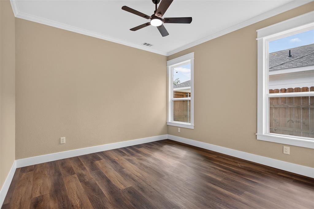 Neutral-toned interior space featuring wood-finish flooring, dual windows with white trim, crown molding, and a ceiling-mounted fan with light fixture