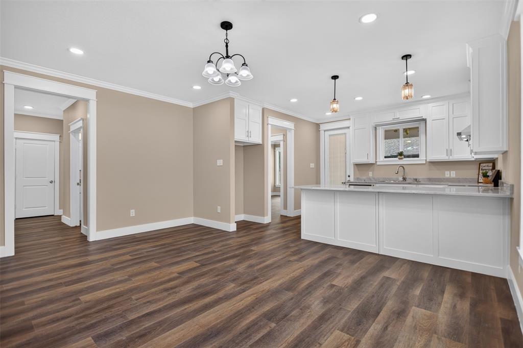 Kitchen area featuring white shaker-style cabinetry, granite countertops, a multi-light chandelier, pendant lighting, and wood-finish flooring