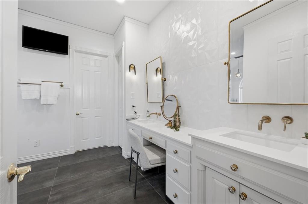Custom white cabinetry with integrated vanity, textured white wall tiling, gold-tone hardware, rectangular undermount sinks, and dark tile flooring