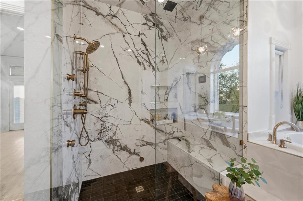 Walk-in shower featuring floor-to-ceiling stone-patterned tile, integrated wall niche, built-in stone bench, and antique-finish hardware with a rainfall showerhead
