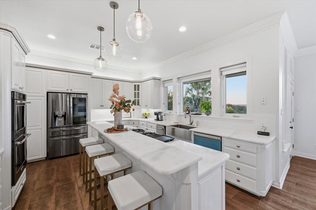 Kitchen featuring white cabinetry, stone-surface countertops, stainless steel appliances, farmhouse sink, and glass pendant lighting