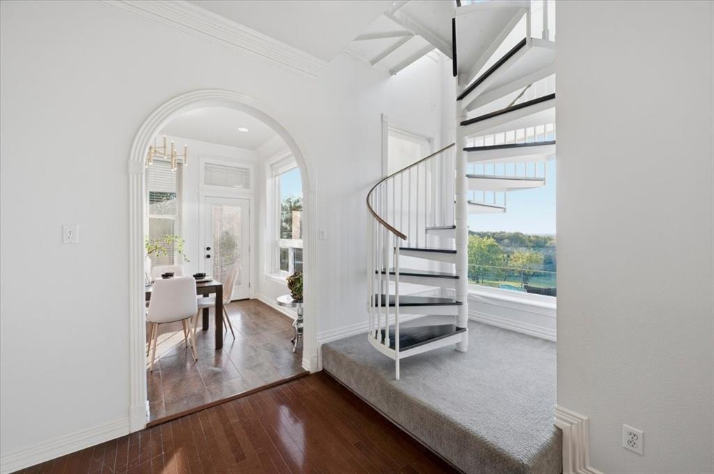 White metal spiral staircase featuring a wood handrail, architectural arched doorway, and wood-finish flooring