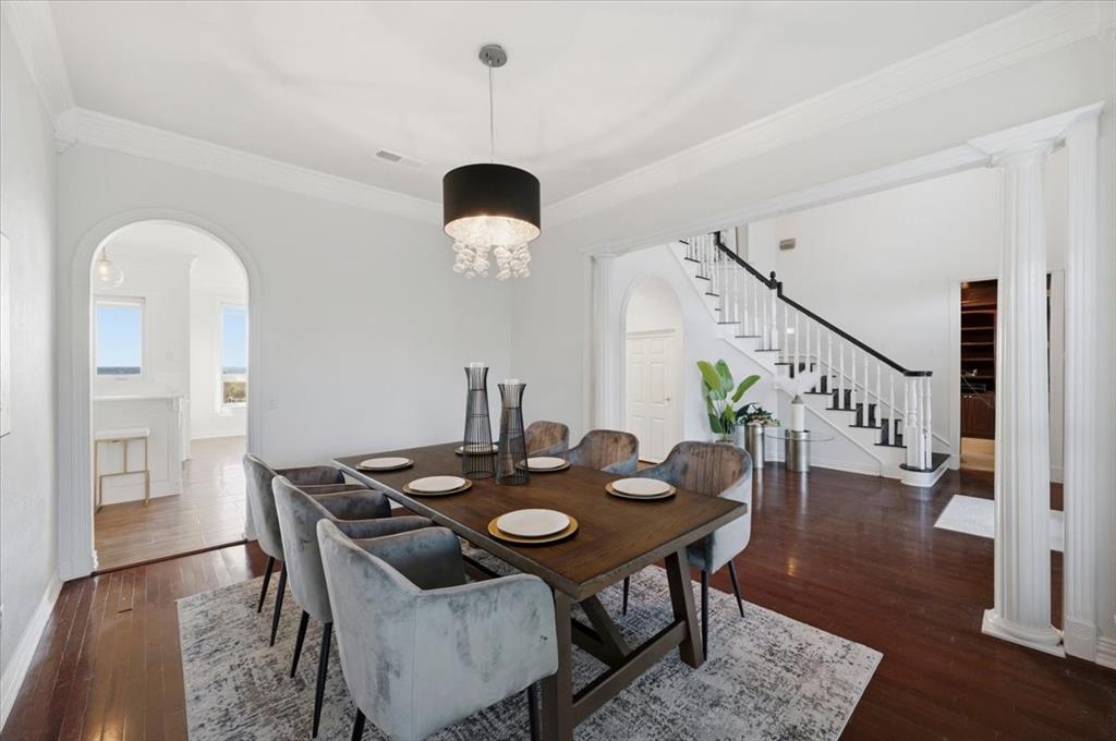 Formal dining area featuring dark wood-finish flooring, a contemporary drum chandelier with crystal accents, crown molding, arched entryways, and a staircase with a black handrail and white balusters