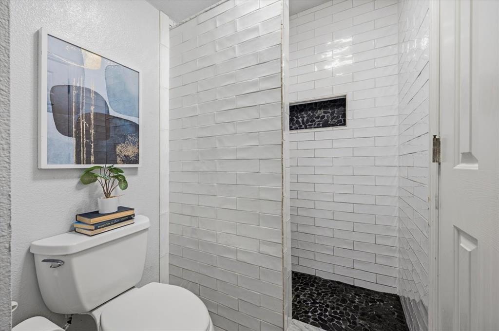 Walk-in shower featuring white subway tile, dark pebble-stone flooring, and a recessed tiled niche
