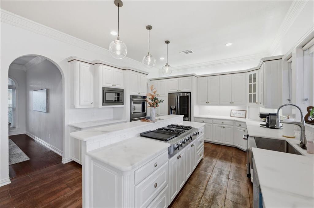 Kitchen featuring white cabinetry, wood-finish flooring, a central island with a cooktop, stone-surfaced countertops, and glass globe pendant lighting
