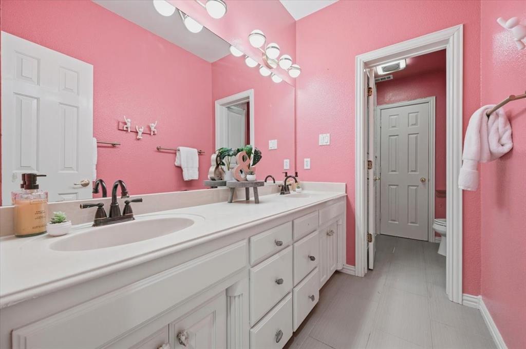 Bathroom featuring a dual-sink vanity with a solid-surface countertop, dark metal hardware, a full-width wall mirror, and a multi-bulb light fixture
