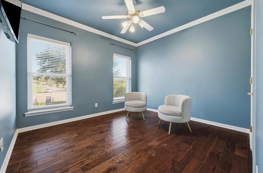 Room featuring wood-finish flooring, dual windows, crown molding, and a central ceiling fan with integrated lighting