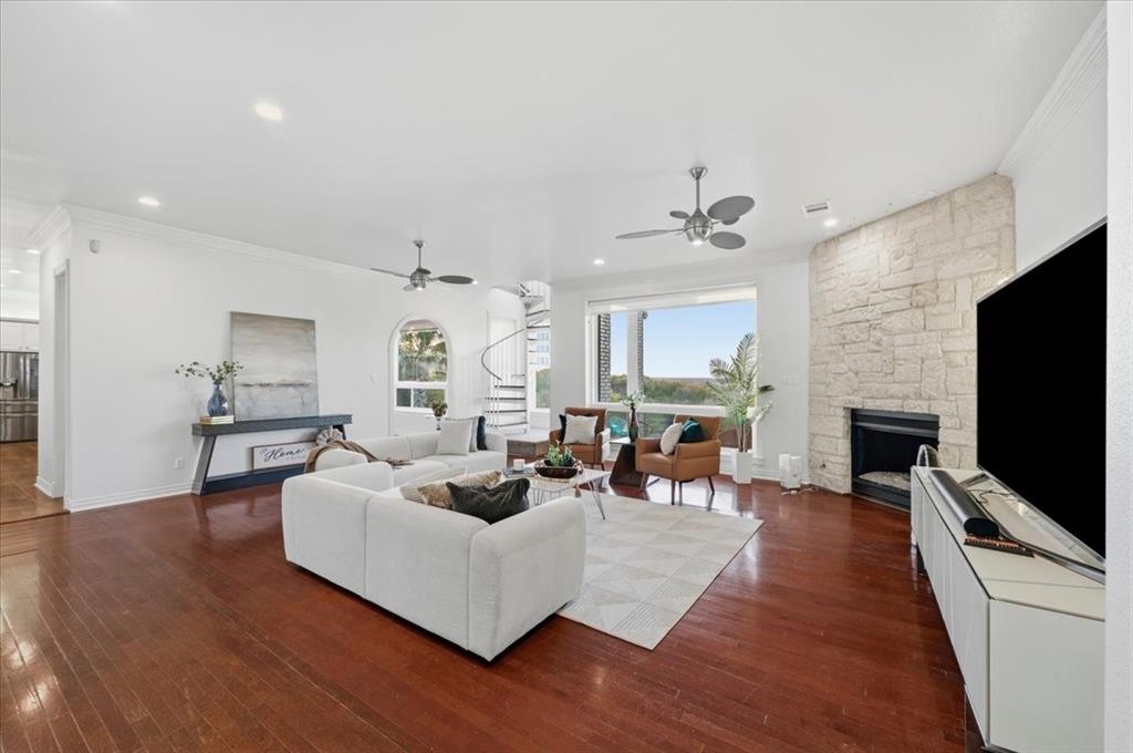 Open-concept living space featuring wood-finish flooring, a full-height stone fireplace, recessed lighting, ceiling fans, and an arched entryway