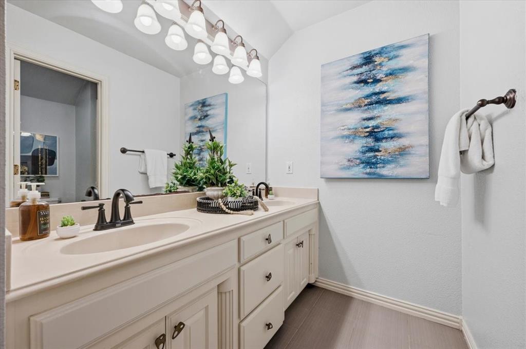 Double vanity featuring white cabinetry, dual integrated sinks with matte black faucets, an expansive wall-mounted mirror, and multi-light overhead vanity fixture