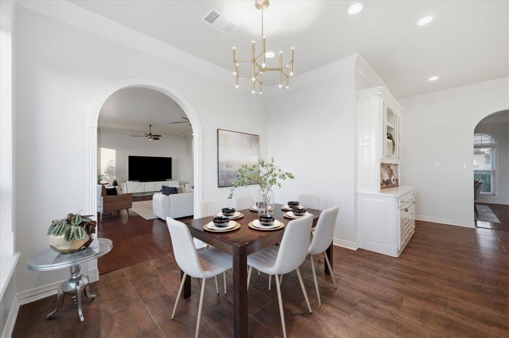Dining space featuring arched entryways, wood-finish flooring, built-in cabinetry, crown molding, and a modern multi-arm chandelier