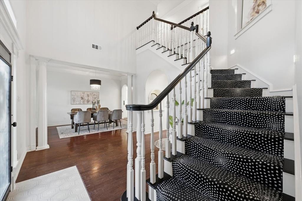 Foyer featuring double-height ceilings, wood-finish flooring, and a staircase with white balusters, a dark handrail, and patterned carpet runner