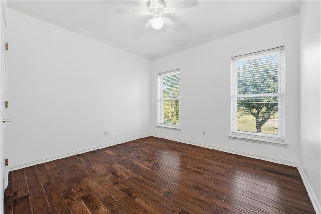 Room featuring wood-finish flooring, dual windows, crown molding, and a central ceiling fan with an integrated light fixture