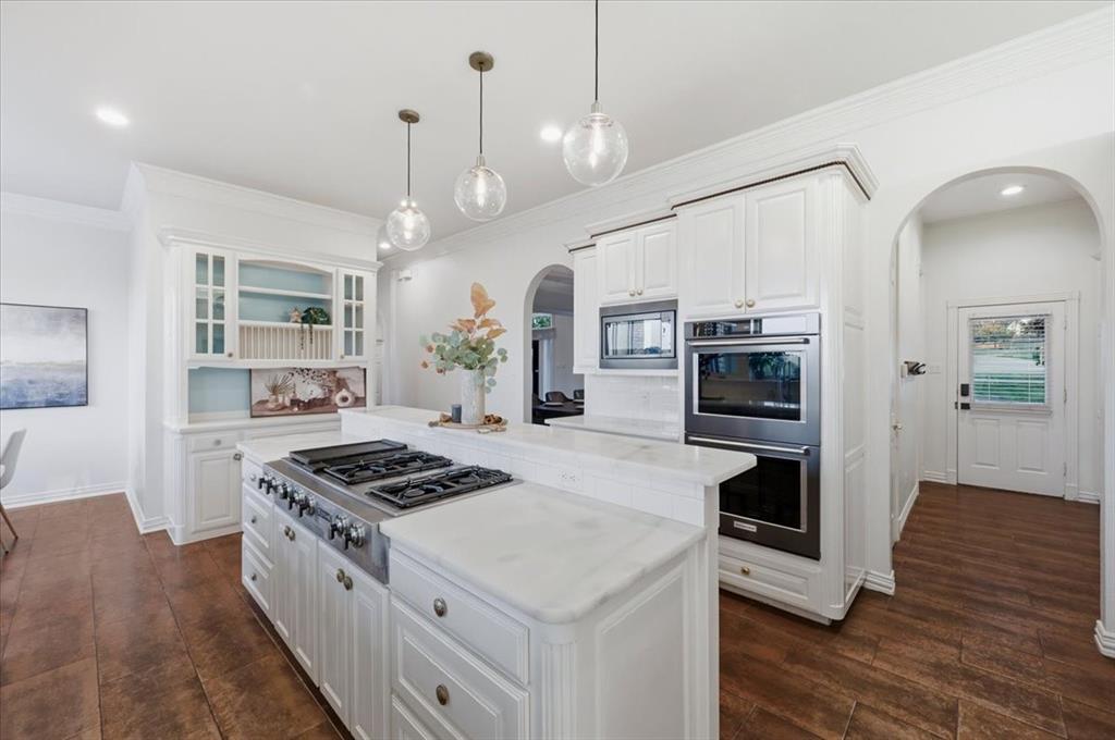 Kitchen featuring white cabinetry, stone countertops, built-in double wall ovens, a gas cooktop, and glass globe pendant lighting