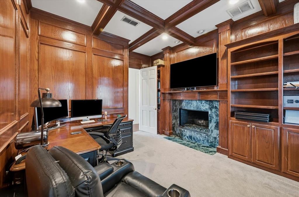 Rich wood-paneled walls and ceiling coffering, custom built-in floor-to-ceiling cabinetry, and a fireplace with a stone surround