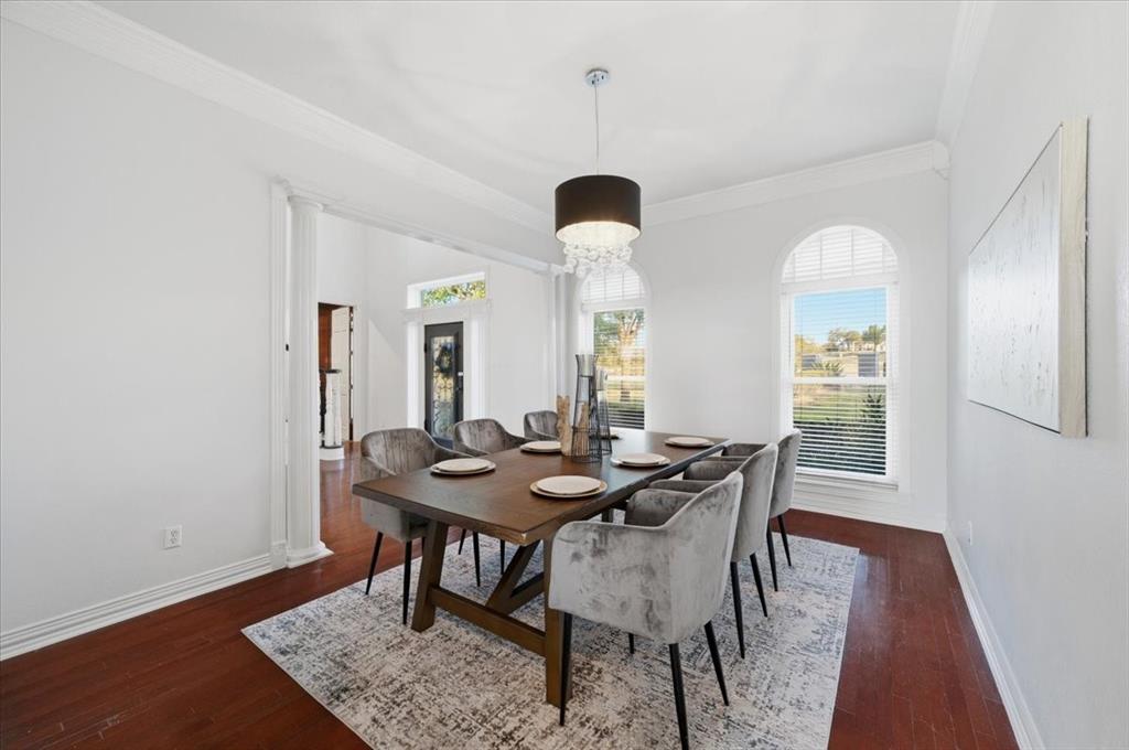 Dining area featuring wood-finish flooring, crown molding, arched windows with plantation shutters, and a drum-style crystal chandelier