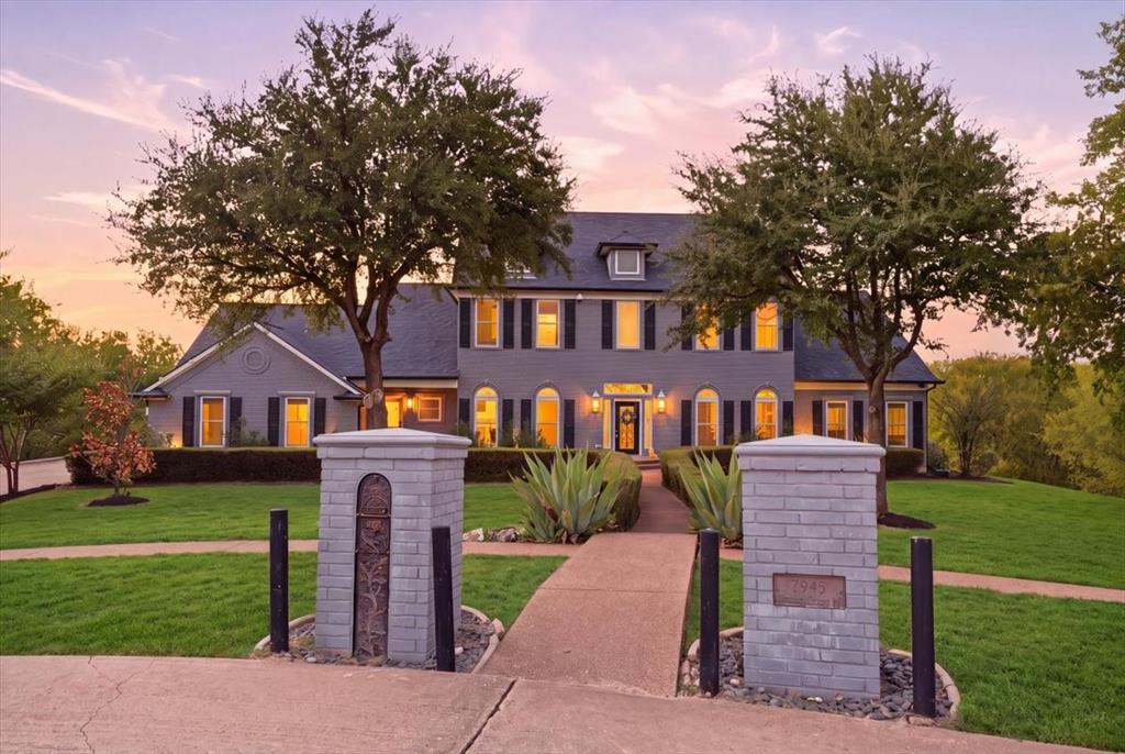 Two-story residence featuring a gray siding exterior, dark shutters, gabled rooflines, decorative brick entry pillars, and mature landscaping