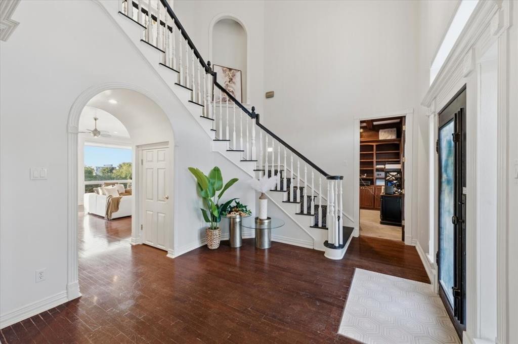 Foyer featuring wood-finish flooring, a staircase with decorative railings, arched architectural openings, an inset wall niche, and built-in cabinetry