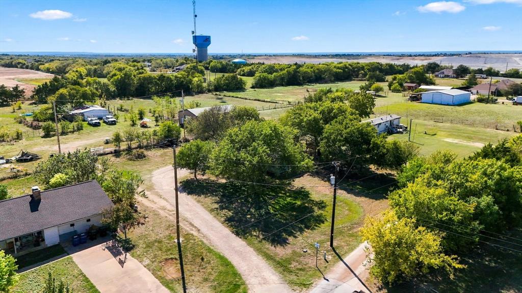 Aerial perspective featuring expansive acreage, mature tree canopy, gravel drive access, and a multi-structure site layout