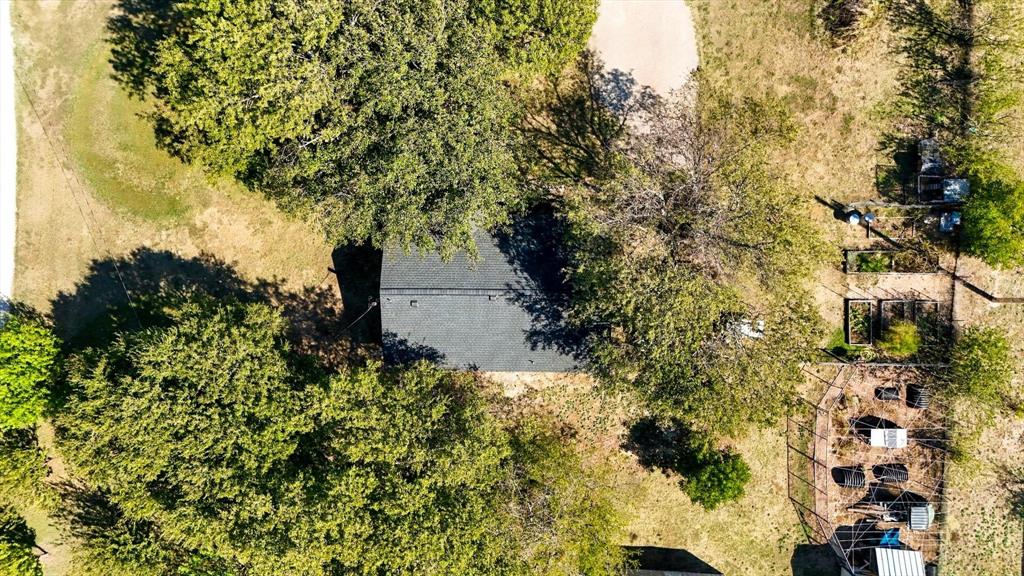 Aerial perspective featuring a shingled roofline, mature trees, open grounds, and a fenced garden area