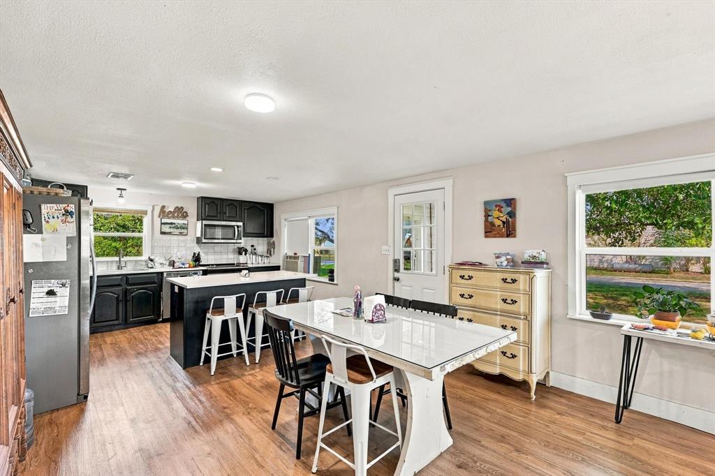 Kitchen featuring black cabinetry, a white central island with counter seating, stainless steel appliances, wood-finish flooring, and multiple windows Kitchen featuring black cabinetry, a white central island with counter seating, stainless steel appliances, wood-finish flooring, and multiple windows
