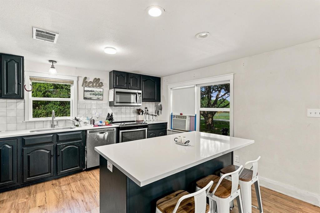 Kitchen featuring dark cabinetry, solid-surface countertops, center island with seating, stainless steel appliances, and wood-finish flooring