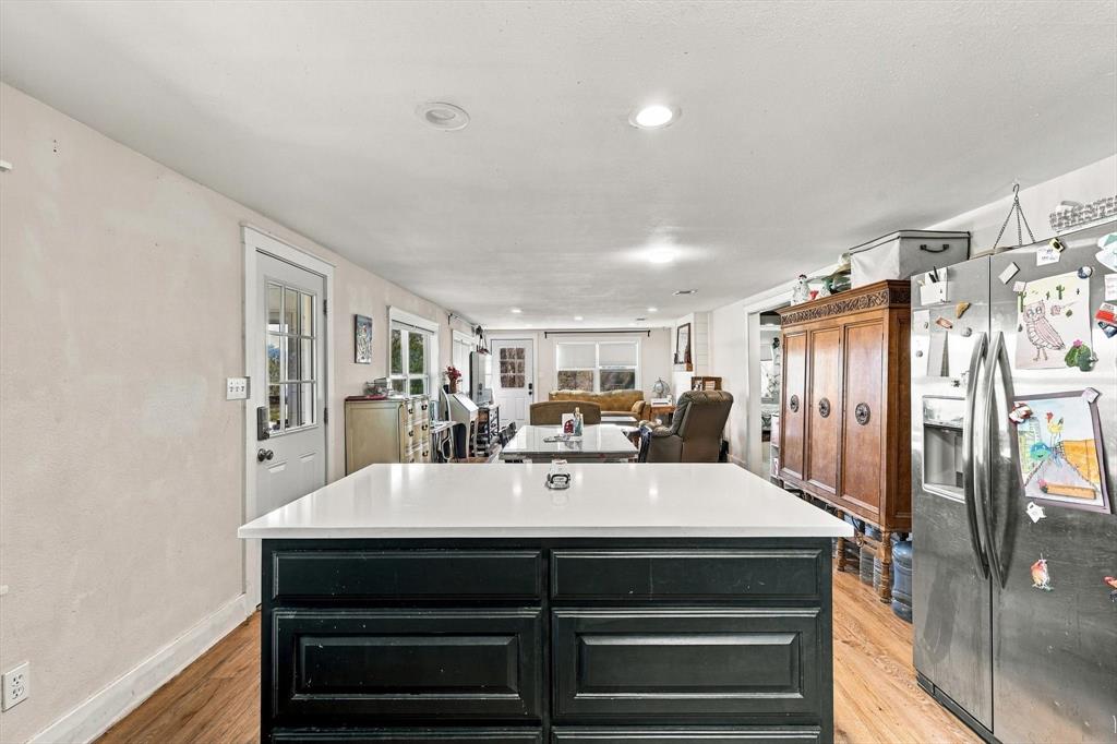 Kitchen island featuring a solid-surface countertop and dark cabinetry, stainless steel refrigerator, recessed lighting, and wood-finish flooring