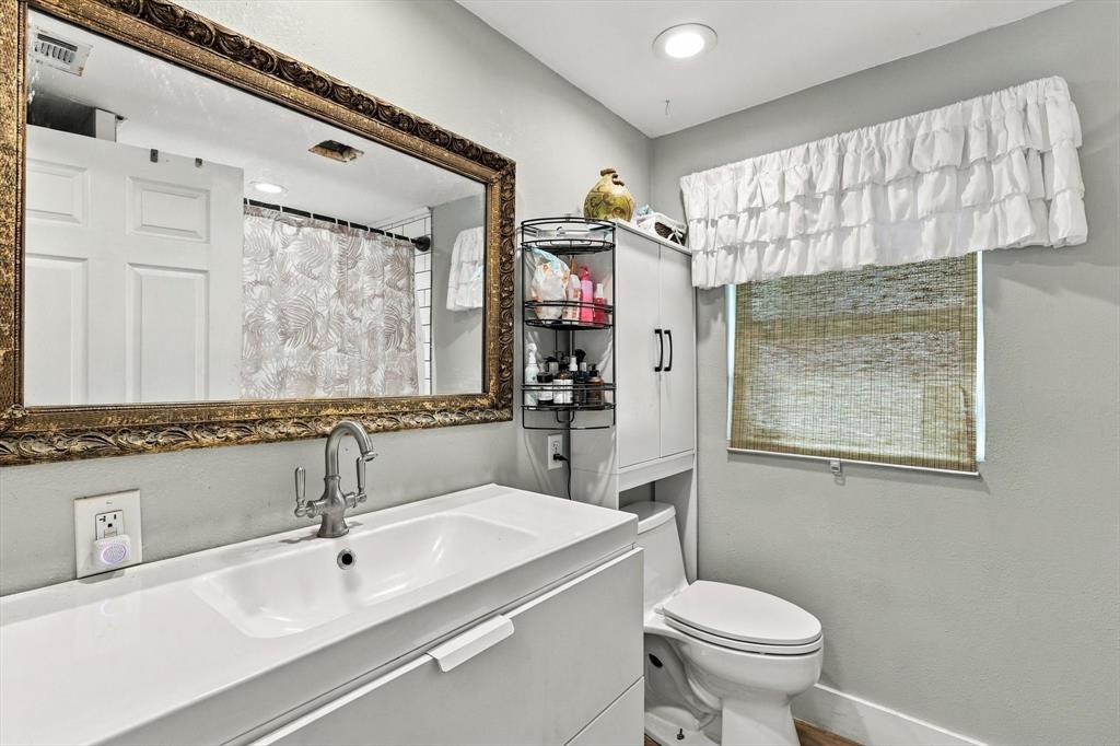 Modern vanity with integrated basin and polished metal faucet, large wall-mounted ornate gold-tone framed mirror, recessed lighting, and built-in vertical storage cabinet